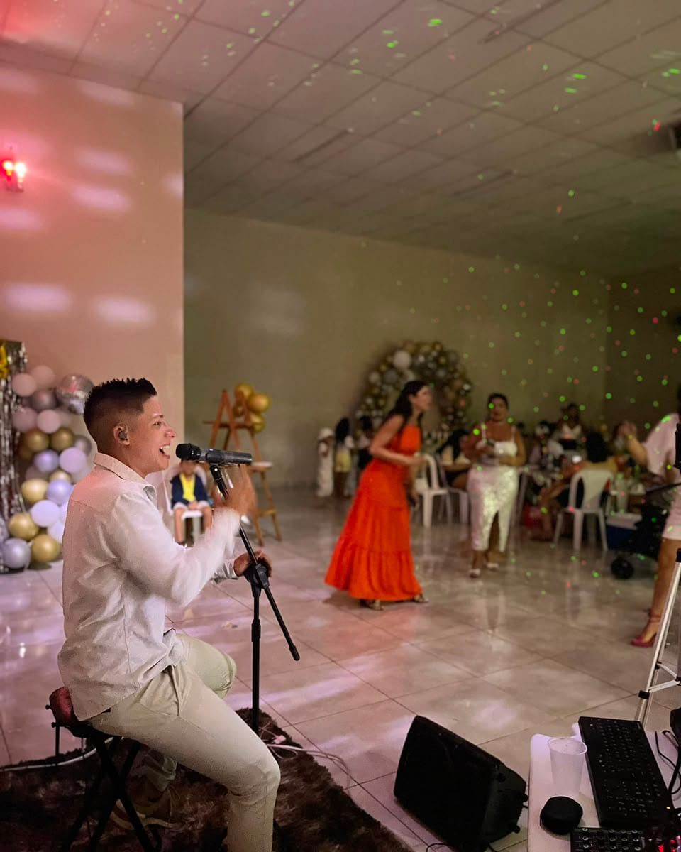 Diego Simonete cantando em uma festa de salão, com o público dançando ao fundo