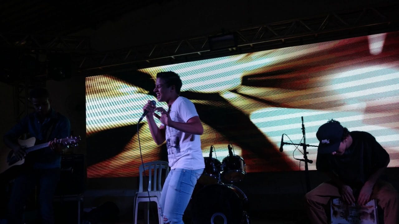 Diego Simonete cantando em palco com painel de LED e banda ao fundo